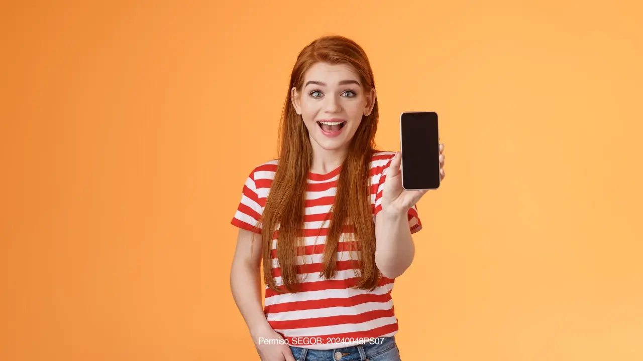 pelirroja feliz mostrando un celular con fondo naranja